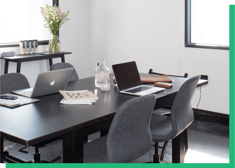 meeting room with 4 office chairs and a black table with two laptops on the table
